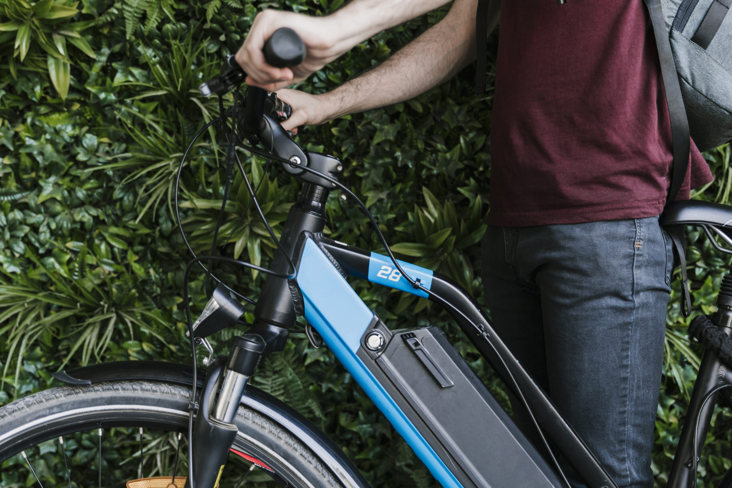Man holding a modern electric bicycle, representing the concept of the Patanjali Electric Cycle, with an eco-friendly green wall background.